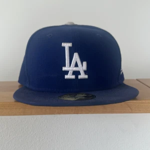 Blå LA Dodgers keps från New Era - Säljer en blå LA Dodgers keps från New Era 59FIFTY med broderad LA-logga framtill och MLB-logga bak. Kepsen har platt skärm och klassisk passform. Kepsen är köpt i LA därav lite extra exklusiv!