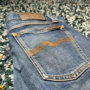 Nudie Jeans Tight Skinny Blå 27/34 - Snygga blå jeans från Nudie Jeans med klassisk orange söm på bakfickan. Modellen är tight och skinny med normal midja. Jeansen är i bomull och har en autentisk tvättad look. Perfekta för dig som gillar en smal passform och stilren design.