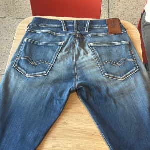 Blå Replay jeans med slitningar - Snygga blå jeans från Replay med slitna detaljer och tydliga kontrastsömmar. Klassisk femficksmodell med läderpatch bak i midjan och broderade bakfickor. Jeansen har en tvättad look och logotypdetalj vid myntfickan. Perfekta för en avslappnad streetstil.