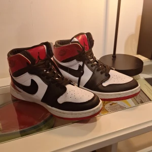 Nike Air Jordan 1 High svart/röd/vit - Tjena säljer ett par Nike Air Jordan 1 High med klassisk färgblockning i svart, rött och vitt. Skorna har snörning, rund tå och röd yttersula. Tillverkade i skinn med ikoniska Jordan Wings-loggan på sidan och Jumpman på plösen. Perfekta för dig som gillar streetwear och sneakerskultur. Använd men inte jätte mycket.