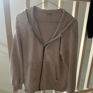 Ljusgrå/vit hoodie med dragkedja - Ljusgrå hoodie från Cubus i storlek 146/152. Tröjan har huva, hel dragkedja framtill och två fickor. Mjuk insida och ribbade muddar vid ärmslut och nederkant. Perfekt för chill dagar eller när du vill vara extra bekväm.