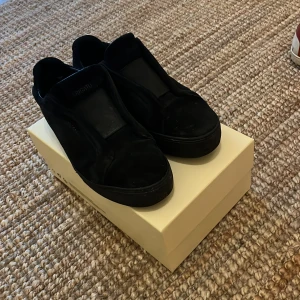 Svarta sneakers från Axel Arigato - Snygga svarta sneakers från Axel Arigato i mocka med minimalistisk design. Skorna har en platt sula, rund tå och diskret logga på sidan. Perfekta för dig som gillar stilrena och trendiga skor med premiumkänsla.