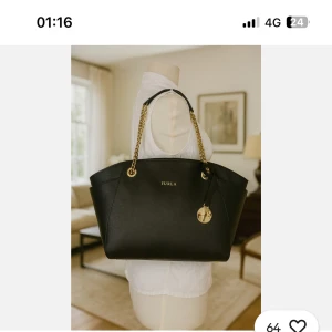 Svart Furla handväska med guldkedjor  - Stilren svart handväska från Furla med eleganta guldfärgade kedjehandtag och Furla-logga framtill. Väskan är rymlig och har en klassisk form, perfekt för dig som vill ha en snygg och praktisk accessoar. Tillverkad i skinn med exklusiva detaljer. Priset kan diskuteras och jag köpte den för 3000