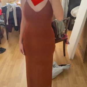 Brun långklänning med smala axelband - Säljer en snygg brun långklänning med smala axelband och v-ringning. Klänningen har en figurnära passform och är perfekt för dig som gillar en stilren och enkel look. Materialet känns mjukt och följsamt mot kroppen.