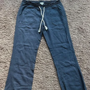 Blå linnebyxor med snörning - Snygga blå linnebyxor ifrån roxy med avslappnad passform och breda ben. Byxorna har resår i midjan och en vit snörning framtill för extra stilpoäng. Perfekta för en chill och bekväm look.