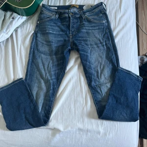 Blå jeans från Jack & Jones - Snygga blå jeans från Jack & Jones med klassisk femficksdesign och slitna detaljer framtill. Jeansen har raka ben och normal passform, tillverkade i mjukt denimtyg. Perfekta för en avslappnad och cool look.