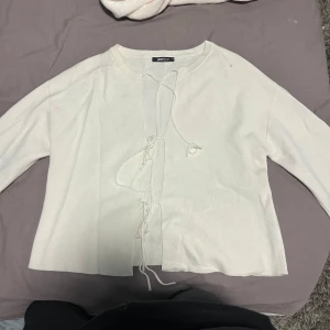 Vit kofta med snörning från Gina Tricot - Supersöt vit kofta från Gina Tricot i stickat material. Koftan har långa ärmar och snygg snörning framtill som ger en trendig touch. Perfekt att slänga över en topp för en chill look. Enkel och stilren design som passar till mycket.