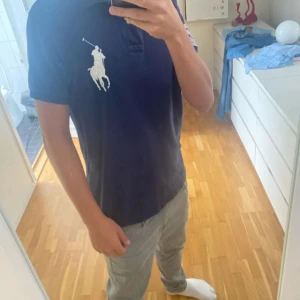 Mörkblå Polo Ralph Lauren Wimbledon pike  - Snygg mörkblå piké  från Polo Ralph Lauren med stor vit polospelare på bröstet och Wimbledon-märke på ärmen. Klassisk krage och knappslå framtill. Custom fit-modell i mjuk bomull, perfekt för dig som gillar sportig stil och tennis.