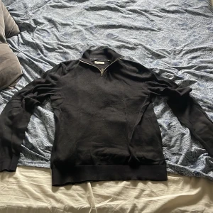 Svart half zip tröja från Jack and Jones - Svart långärmad tröja från Jack & Jones med half zip-dragkedja vid halsen. Tröjan har en klassisk, stilren look med ribbade muddar och är tillverkad i mjukt material som passar perfekt för kyliga dagar. Snygg att matcha med jeans eller chinos. S men passar även M