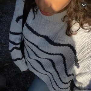 Vit stickad randig tröja - Säljer en vit stickad tröja med blåa  ränder. Tröjan har en rund hals och långa ärmar, perfekt för dig som gillar en chill och stilren look. Materialet är kabelstickat och ger en skön känsla. Passar dig som vill ha en enkel men snygg tröja.
