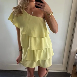 Gul omlottklänning med volanger - KOM MED PRISFÖRSLAG!! Säljer en ljusgul kortklänning med flera lager volanger och oneshoulder-design. Klänningen har en luftig och flowy passform, perfekt för sommarens varma dagar. Materialet känns lätt och svalt mot huden och ger en fräsch vibe. Väldigt populär och trendig.