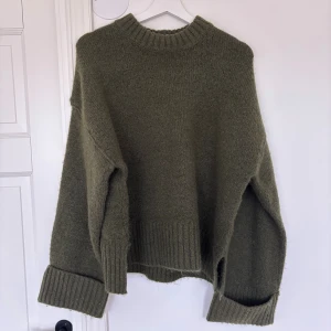 Olivgrön stickad tröja Gina Tricot - Mysig olivgrön stickad tröja från Gina Tricot i storlek S. Tröjan har en rund hals, breda ribbade muddar och lång ärm med loose passform. Perfekt för att hålla sig varm och se chill ut under kyliga dagar. Använd endast en gång!