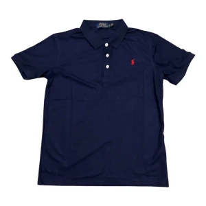 Marinblå pikétröja från Polo Ralph Lauren - Snygg marinblå pikétröja från Polo Ralph Lauren med klassisk krage och tre vita knappar framtill. Tröjan har korta ärmar och den ikoniska röda broderade loggan på bröstet. Perfekt för en clean och sportig look.