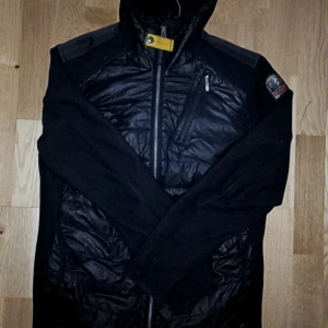 Svart pufferjacka från Parajumpers riktigt fin - Svart pufferjacka från Parajumpers med quiltad front och huva. Jackan har en gul detalj vid halsen, dragkedjor på bröstet och sidan samt ett snyggt Parajumpers-märke på ärmen. Materialmix med polyester och syntet, perfekt för kyliga dagar. Tagit väl hand om den fick den i present för 2 år sen nypris 4999  st S/m så klart äkta !