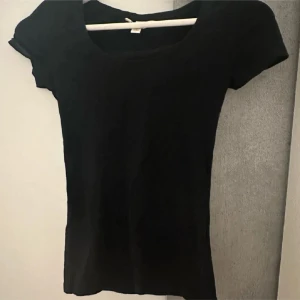 Svart t-shirt från HM i st XS - En enkel svart t-shirt i figurnära passform med rund hals och korta ärmar. Perfekt för dig som gillar en clean och stilren look. Materialet är mjukt och stretchigt, troligtvis bomull eller en bomullsblandning. Passar dig som vill ha en basic topp i garderoben.
