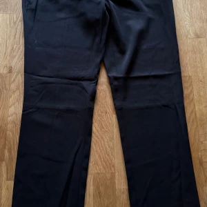 Svarta kostymbyxor från Mexx, strl 42 - Snygga svarta kostymbyxor från Mexx i storlek 42. Byxorna har raka ben, klassisk passform och två bakfickor med lock. Materialet är en mix av polyester, viskos och elastan för en skön känsla och bra stretch. Perfekta för en clean och stilren look.