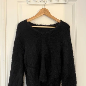 Svart fluffig stickad tröja - Mysig svart stickad tröja med fluffig yta och rund hals. Perfekt för dig som gillar en chill och skön stil. Tröjan har långa ärmar och en loose passform som gör den extra bekväm. Passar dig som vill ha en enkel men ändå trendig look.