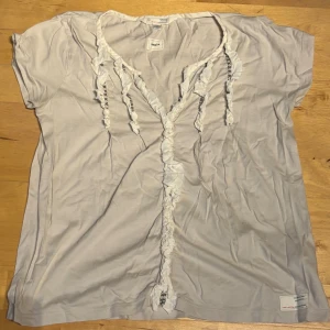 Vit/beige blus med volang från Odd Molly - Säljer en vit/beige blus från Odd Molly med korta ärmar och v-ringad hals. Blusen har dekorativa volanger och broderade detaljer längs halsringningen och framtill. Mjuk bomullskvalitet som känns skön mot huden. Perfekt för dig som gillar en romantisk och avslappnad stil.