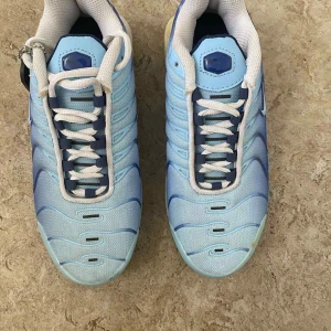 Nike Air Max Plus Tn blå sneakers - Nike Air Max Plus Tn sneakers i ljusblå och marinblå färg med vita detaljer. Skorna har en mesh- och syntetöverdel, vit snörning och en unik Tn Air-dämpad sula. Säljs med Foot Locker-tag. Snyggt vågigt mönster och rund tå.