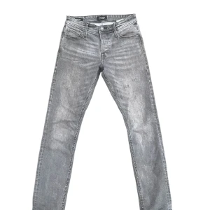 Grå jeans från Jack & Jones - Snygga grå jeans från Jack & Jones med klassisk femficksdesign och raka ben. Jeansenhar tecken på användning som är skapta i fabrik! De är ett otroligt bra val då de är extremt stilrena och kostar mindre än hälften än vad motsvarigheten Nudie eller Replay kostar.