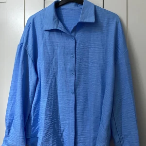 Blå oversized skjorta med knappar - Har beställt från shein men har aldrig använt och som ni ser den är helt nytt med inga skada eller fläckar. Länden till tröjan är 70cm och bredden (från ena axeln till den andra) är 70cm.