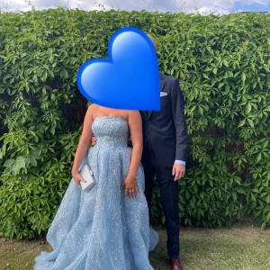 Blå glittrig balklänning med snörning - Magisk blå långklänning med glittriga paljetter över hela tyget och snygg snörning i ryggen. Klänningen är axelbandslös och har en vid, prinsessliknande kjol som ger en riktigt lyxig känsla. Perfekt för bal eller student! Materialet är troligtvis polyester med glitterdetaljer. Något sliten under till men inget som syns. 