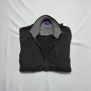 Cardigan Sand - Mörkgrå kofta från Sand Pink Label med hel dragkedja och ribbade muddar i storlek M-L.  Insidan av kragen har ett snyggt randigt mönster i grått och vitt. Materialet är stickad bomull, perfekt för lager på lager. Klassisk och chill look med långärmad passform.                                                                            Tveka inte att höra av dig vid minsta fundering!