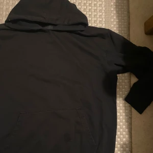 Svart hoodie med huva och ficka - Svart hoodie med klassisk huva och stor magficka framtill. Tröjan har långärmade ärmar och är gjord i mjukt bomullsmaterial, perfekt för chill dagar eller när du vill ha något bekvämt. Enkel och stilren design som funkar till det mesta.