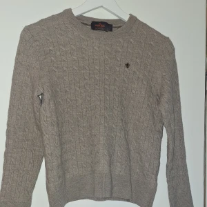 Beige kabelstickad tröja Morris L - Kabelstickad beige tröja från Morris i 100% merinoull. Rund hals, ribbade muddar och diskret broderad logga på bröstet. Perfekt för dig som gillar klassisk stil med en modern touch. Kvaliten på tröjan är 10/10 och passar dig som är runt 150. Skriv om du har några funderingar.
