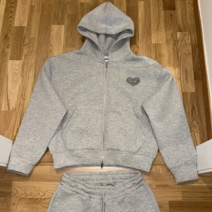 Grå mjukisbyxor från StreetSpirit  - Snygga grå mjukisbyxor från StreetSpirit koftan är storlek XS och byxorna är storlek S Byxorna har normal passform, elastisk midja med snörning och ett broderat hjärta med öga på fickan. Mjukt bomullsmaterial som är perfekt för chill dagar. Matcha med hoodien för en komplett look.