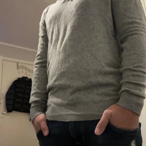  half zip - grå tröja med ribbad krage och halv dragkedja framtill. Tröjan är långärmad och har en klassisk, stilren look som passar perfekt till jeans eller chinos. Mjuk och skön, perfekt för kyligare dagar.