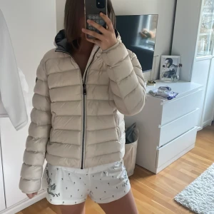 Beige pufferjacka från Colmar - Säljer en beige pufferjacka från Colmar Originals med huva och snygga breda kanaler. Jackan har dragkedja framtill och Colmar-logga på ärmen. Insidan är mörkgrå och materialet är polyester. Perfekt för dig som vill ha en clean och modern look.