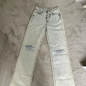 Ljusa raka jeans med slitningar - Säljer ett par ljusa jeans med raka ben och snygga slitningar vid knäna. Klassisk femficksmodell och hög midja. Perfekt för dig som gillar en avslappnad och trendig stil.