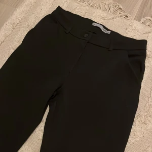 Svarta kostymbyxor med raka ben - Snygga svarta kostymbyxor från lager 157 med klassisk rak passform och bälteshällor. De är även midwest. Byxorna har knapp och dragkedja framtill samt diskreta fickor. Perfekta för en stilren look och passar dig som gillar enkel och clean stil.