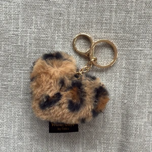 Leopardmönstrad pälsig nyckelring - Supergullig hjärtformad nyckelring från Tinka i mjuk fuskpäls med leopardmönster. Nyckelringen har guldfärgad metall och är perfekt att hänga på väskan eller använda till nycklarna för en extra touch.
