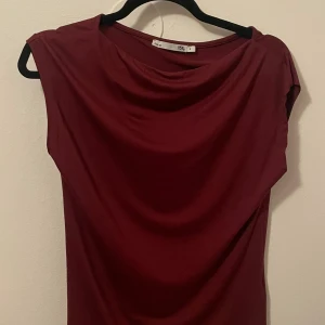 Vinröd topp från lager 157 - Supersnygg vinröd topp från lager 157 med mjukt, slätt tyg och draperad halsringning. Ärmlös design som ger en clean och modern look. Perfekt för dig som gillar stilrena plagg med lite edge.