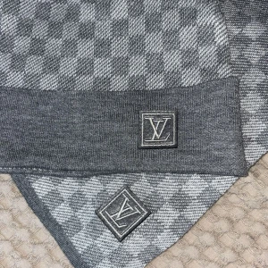 Grå rutig halsduk från Louis Vuitton - Snygg grå halsduk från Louis Vuitton med klassiskt rutigt mönster och LV-logga på kanten. Tillverkad i mjuk kashmir som känns lyxig och varm. Perfekt accessoar för att lyfta din vinterstil med exklusiv känsla.
