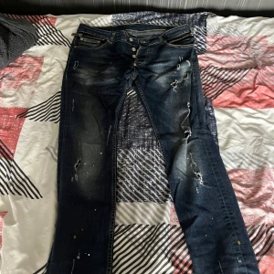 Dsquared2 mörkblå distressed jeans - Säljer ett par snygga mörkblå jeans från Dsquared2 med slitningar, färgstänk och detaljerade dragkedjor vid fickorna. Jeansen har knäppning framtill och klassisk femficksdesign. Pris kan diskuteras om det behövs.