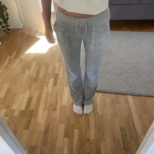 Grå mjukisbyxor Juicy Couture S - Snygga grå mjukisbyxor från Juicy Couture i storlek S. Byxorna har snörning i midjan, raka ben och två bakfickor med lock och knappar. Mjukt material som är skönt att ha på sig, perfekt för chill dagar.