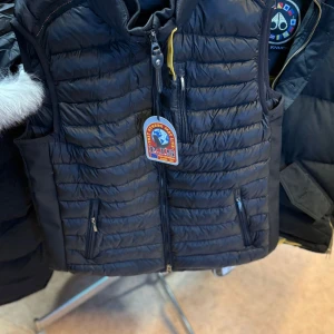 Svart dunväst från Parajumpers - Snygg svart dunväst från Parajumpers med klassisk logga på bröstet och nacken. Västen har quiltad design, dragkedja framtill och praktiska fickor med dragkedja. Perfekt för lager-på-lager och har en sportig vibe med coola detaljer och gul insida vid kragen.