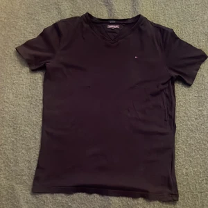 Svart t-shirt Tommy Hilfiger - Blå t-shirt från Tommy Hilfiger i ekologisk bomull. Klassisk v-ringad modell med korta ärmar och diskret logga på bröstet. Snygg och enkel design som funkar till det mesta. Perfekt för dig som gillar stilrena plagg med premiumkänsla.