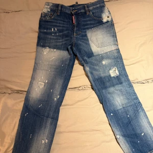 DSQUARED2 blå jeans med slitningar - Säljer ett par blå jeans från DSQUARED2 i storlek 36. Jeansen har coola slitningar och blekta detaljer, klassisk femficksmodell och knappgylf. Materialet är jeans och de har en relaxed vibe med patchade partier och råa kanter.