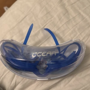 Blå simglasögon från Ocean - Snygga blå simglasögon från Ocean i plast med justerbart band. Perfekta för dig som vill ha klara linser och en cool look i vattnet. Kommer i ett smidigt fodral som skyddar glasögonen när de inte används.