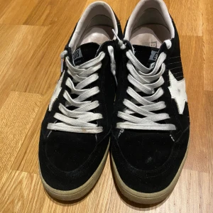 Golden Goose Ball Star svarta sneakers - Svarta Golden Goose Ball Star sneakers i mocka med vit stjärndetalj på sidan och vita snören. Klassisk låg modell med beige sula och rund tå. Snygg kontrast mellan svart och vitt, perfekt för dig som gillar streetstyle och unika detaljer.