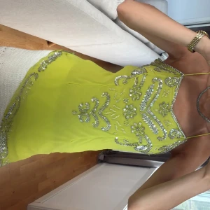 Limegrön blus/kortklänning med paljetter - Säljer en superfin limegrön kortklänning med tunna axelband och detaljerade silvriga paljetter i blommönster framtill. Klänningen har en snygg, figurnära passform och är perfekt för dig som vill sticka ut med färg och glitter. Materialet känns lätt och luftigt.
