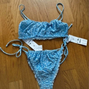 Blommig ljusblå bikini från Gina Tricot - Supersöt ljusblå bikini från Gina Tricot med små vita blommor. Både överdel och underdel har snygga snörningsdetaljer i sidorna och en rynkad design som ger en trendig look. Perfekt för strandhäng och poolparty i sommar!