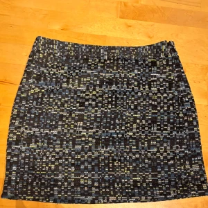 Mönstrad kortkjol från LOFT - Säljer en snygg kortkjol från LOFT med coolt vävt mönster i svart, blått och inslag av gult. Kjolen har rak passform och är fodrad på insidan för extra komfort. Perfekt för dig som gillar unika detaljer och vill sticka ut lite extra.