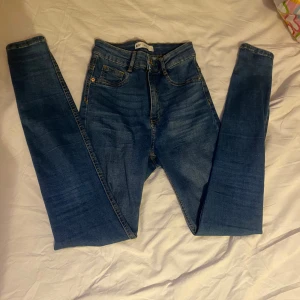skinny Jeans  - Säljer ett par blå Molly jeans från Gina Tricot i storlek S. De är högmidjade och har en skinny passform med klassisk femficksdesign och gul kontrastsöm. Jeansen är tillverkade i stretchigt denim för en bekväm känsla.