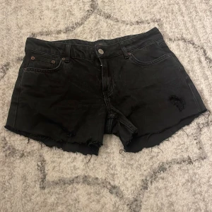 Svarta jeansshorts från NLY - Svarta jeansshorts från NLY med råa, fransiga kanter och slitna detaljer. Klassisk femficksmodell med knapp och dragkedja framtill. Perfekta för en edgy sommarlook.