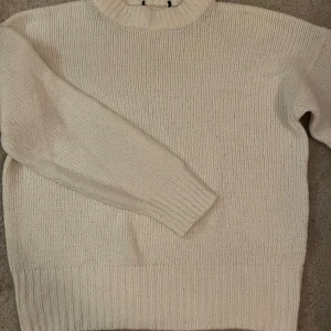 Vit stickad tröja med hög krage - Mysig vit stickad tröja med hög ribbad krage och långa ärmar. Perfekt för kyliga dagar och enkel att matcha med jeans eller kjol. Tröjan har en klassisk rak passform och breda ribbade muddar vid ärmslut och nederkant.